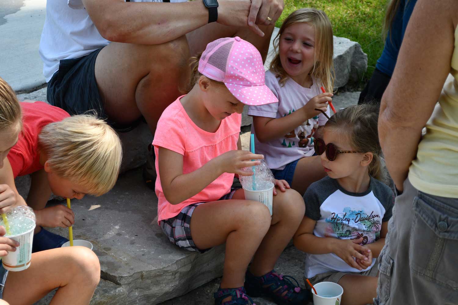 A group of kids sitting on outdoor steps creating bubbles by blowing in a straw in a cup.