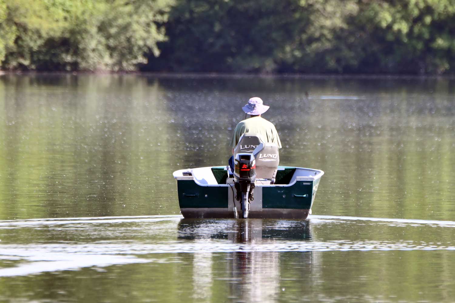Person riding in a boat heading towards a tree line.