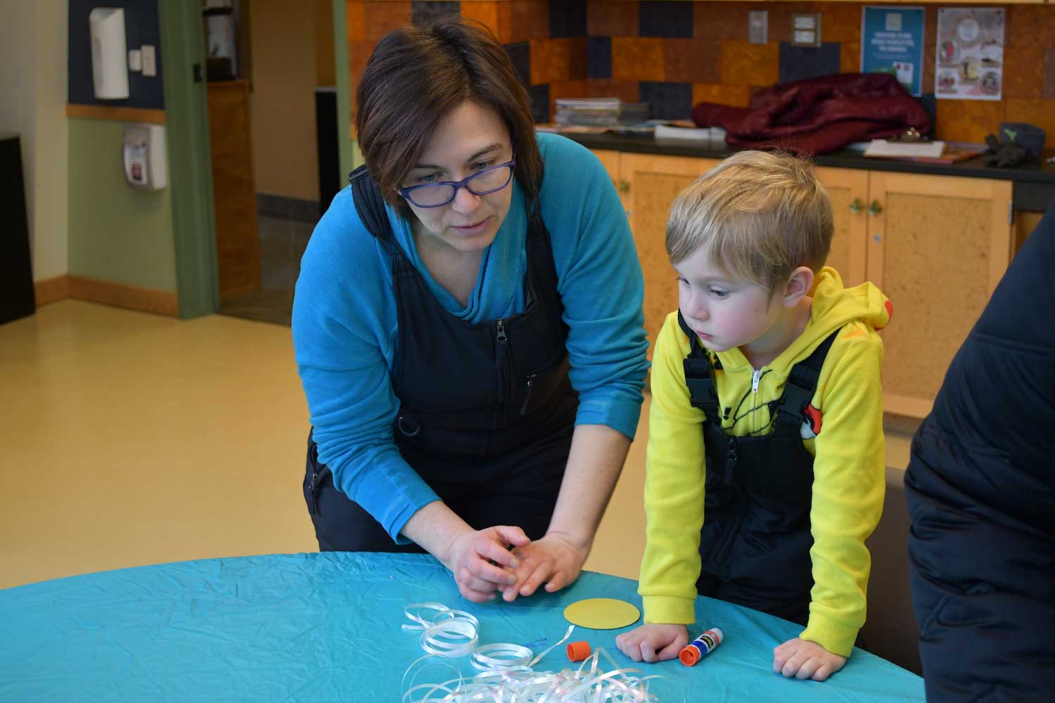 An adult and child looking down at a table covered with craft supplies.