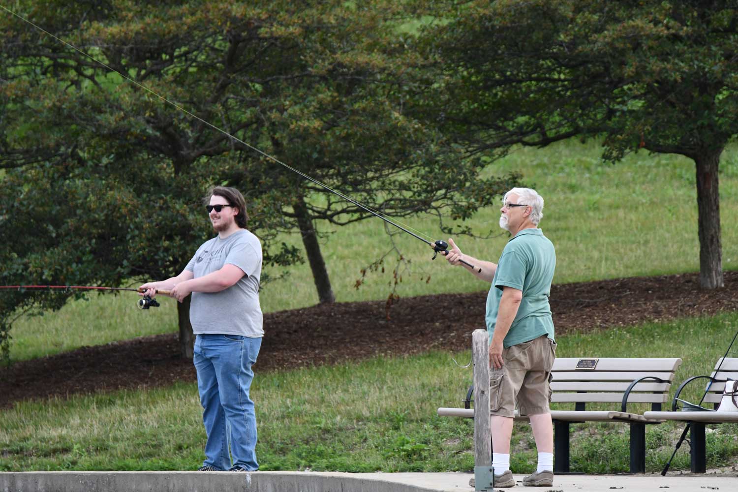 Two people standing along the shore fishing in a lake.