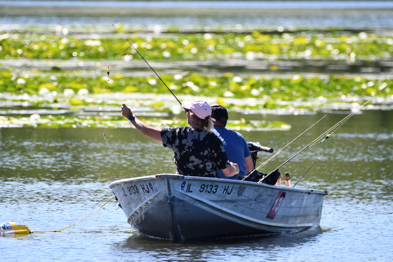 Two people in a small fishing boat on a lake. Both are maneuvering fishing poles.