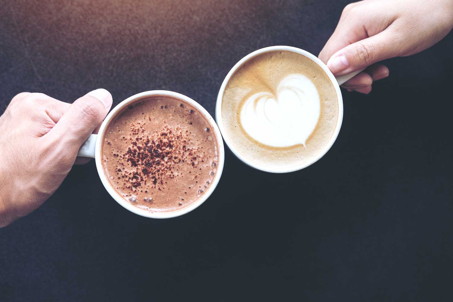 Hands holding cups of coffee and hot cocoa.