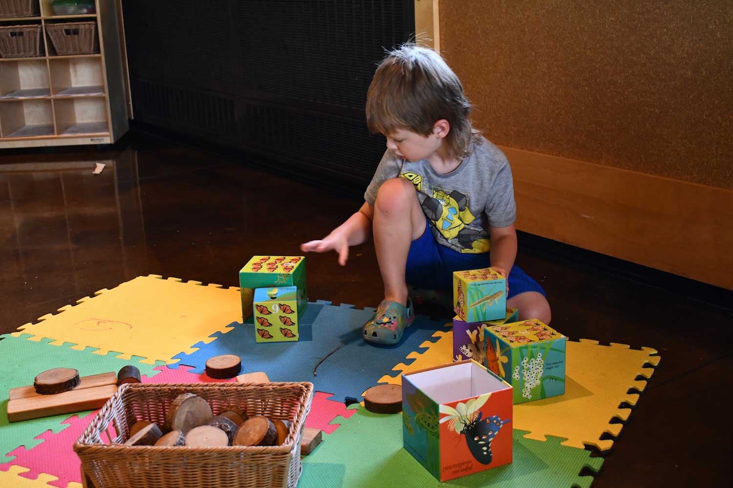 A child sitting on a play mat playing with stackable blocks.