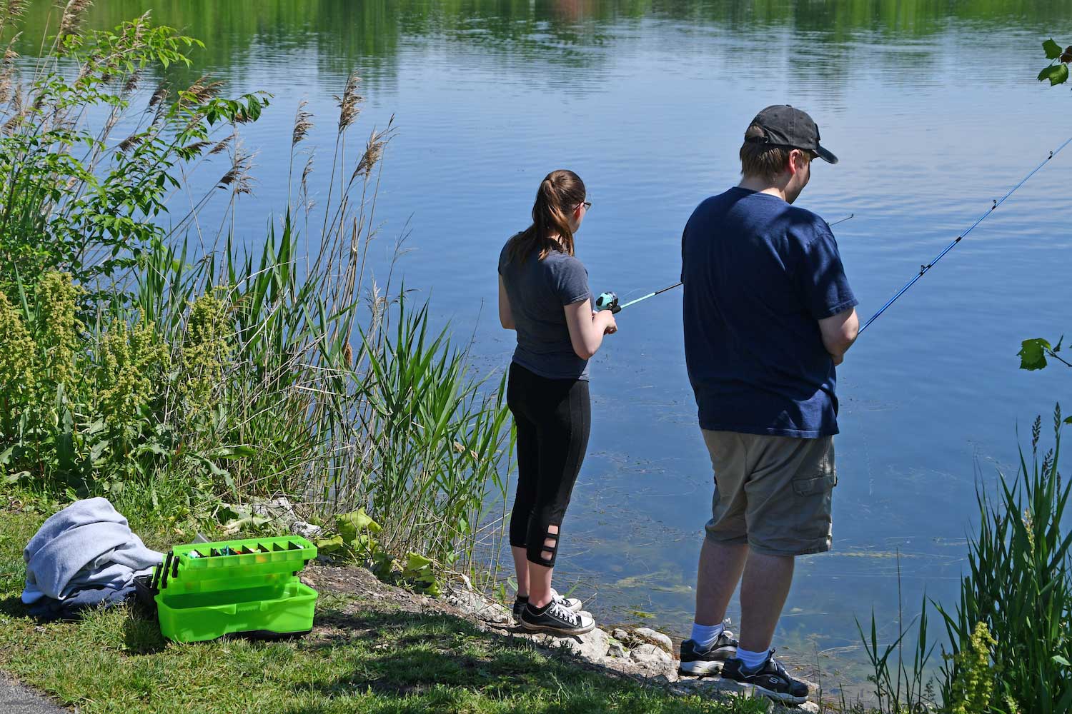 A man and a woman standing along a shoreline fishing.