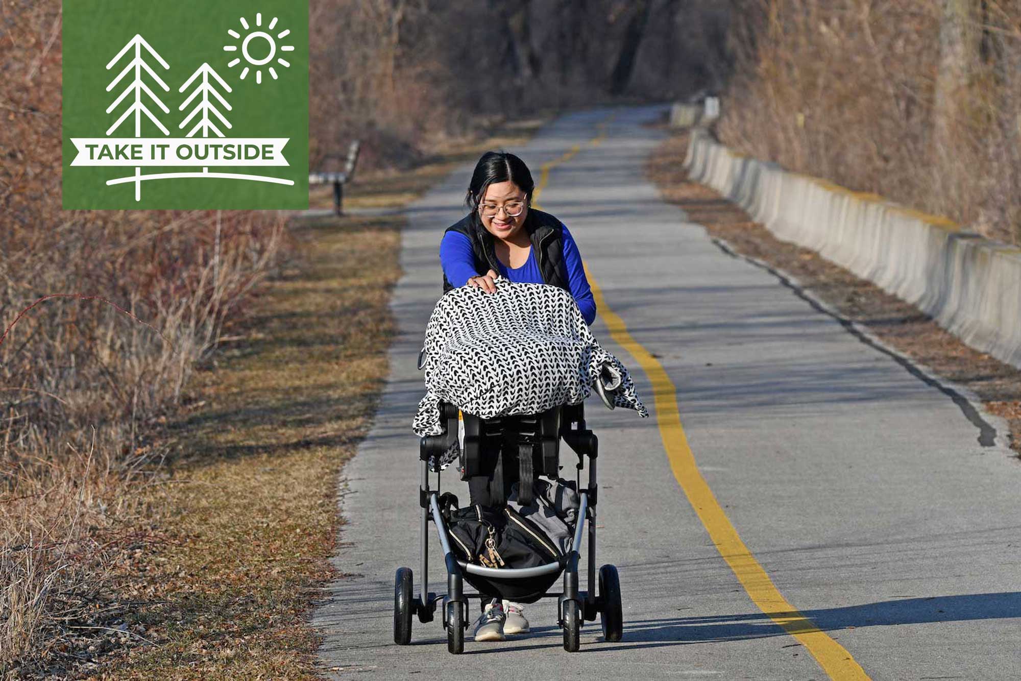 A woman pushing a stroller on a paved trail.