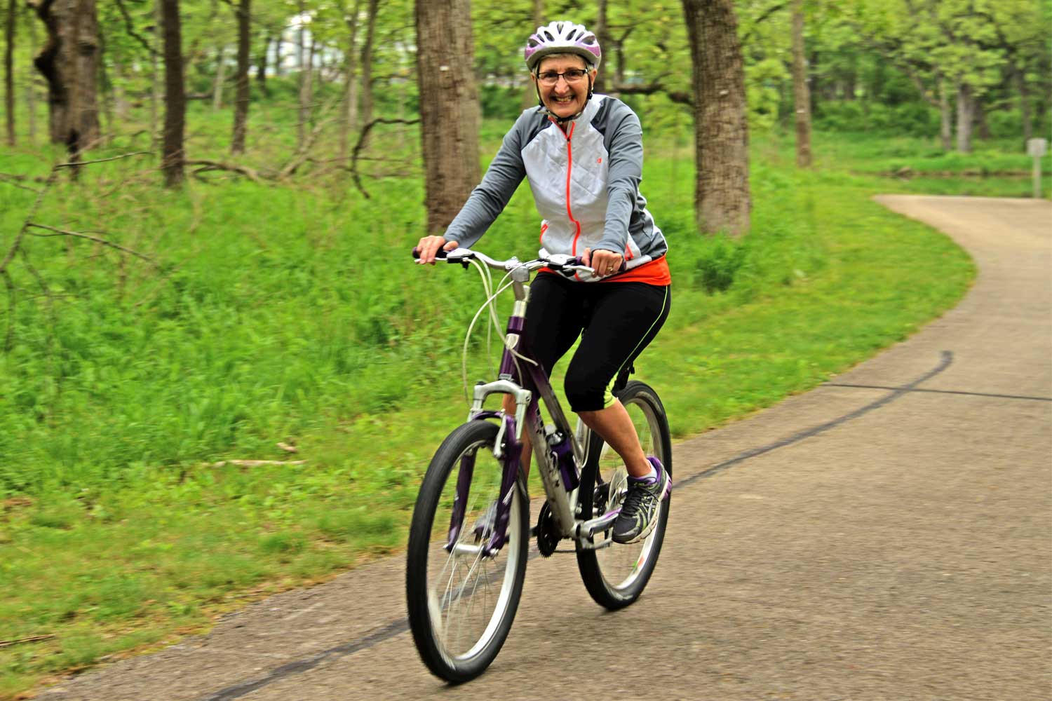 Person with helmet on biking along a paved trail and smiling.