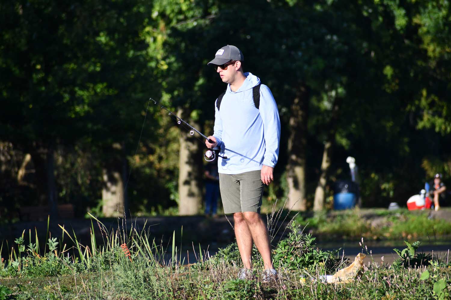 A person wearing a backpack and holding a fishing pole while fishing along a shoreline.