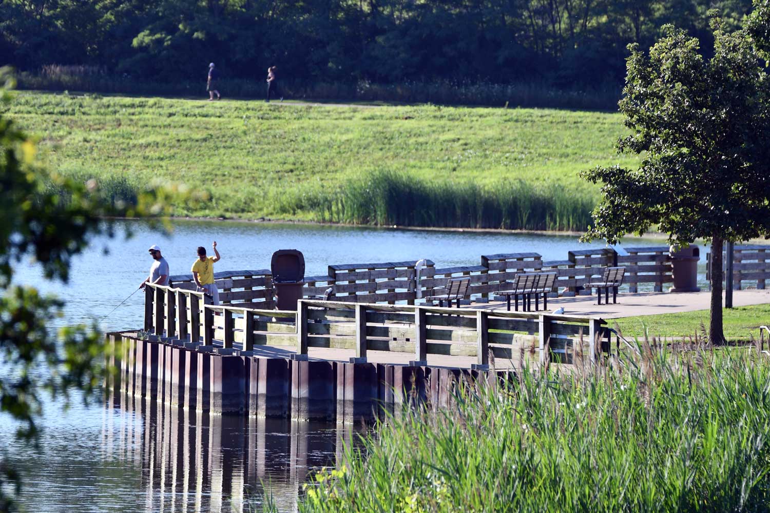 Two people fishing along a paved shoreline trail. 