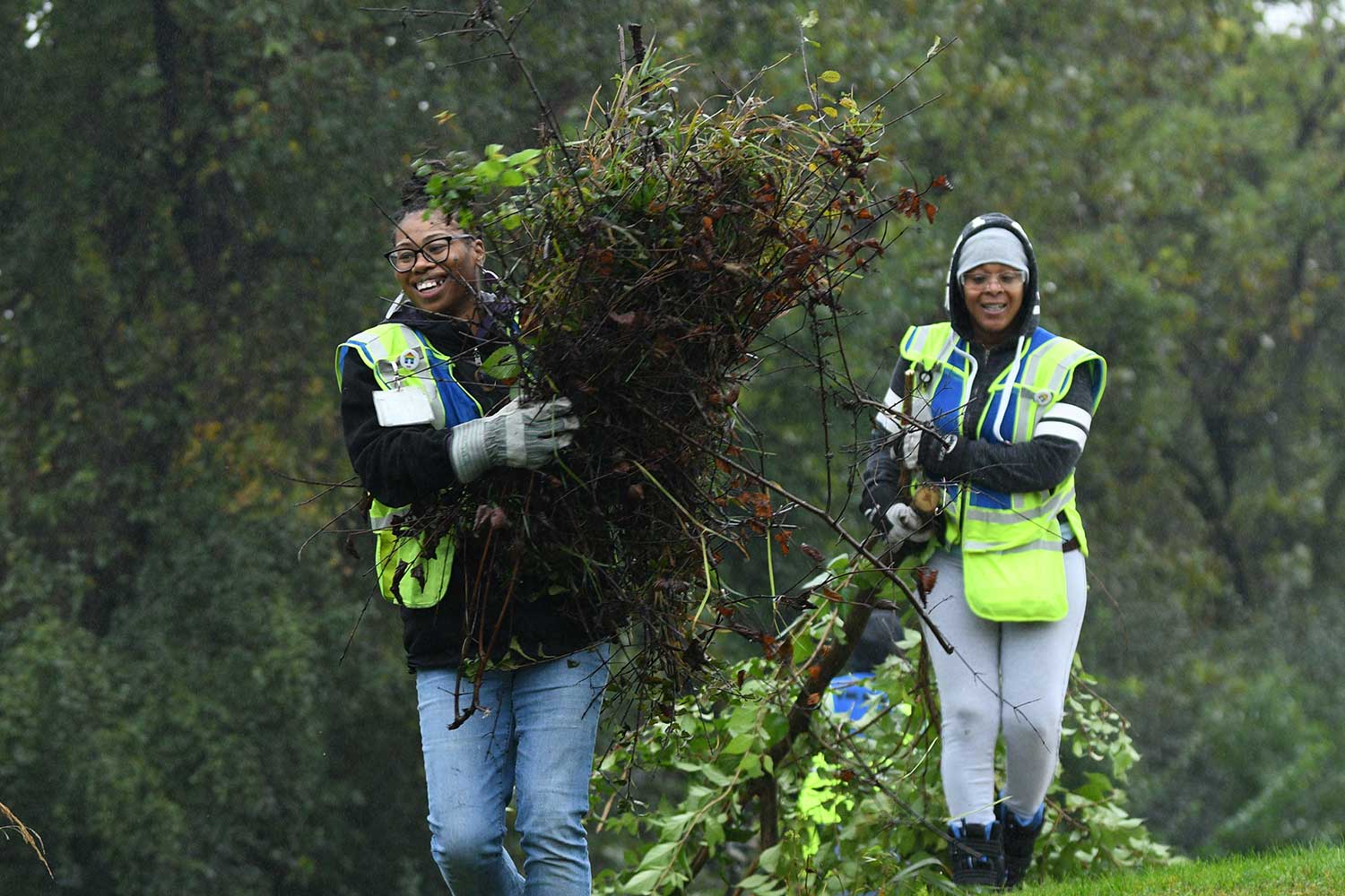 Two people hauling branches and armfuls of brush.