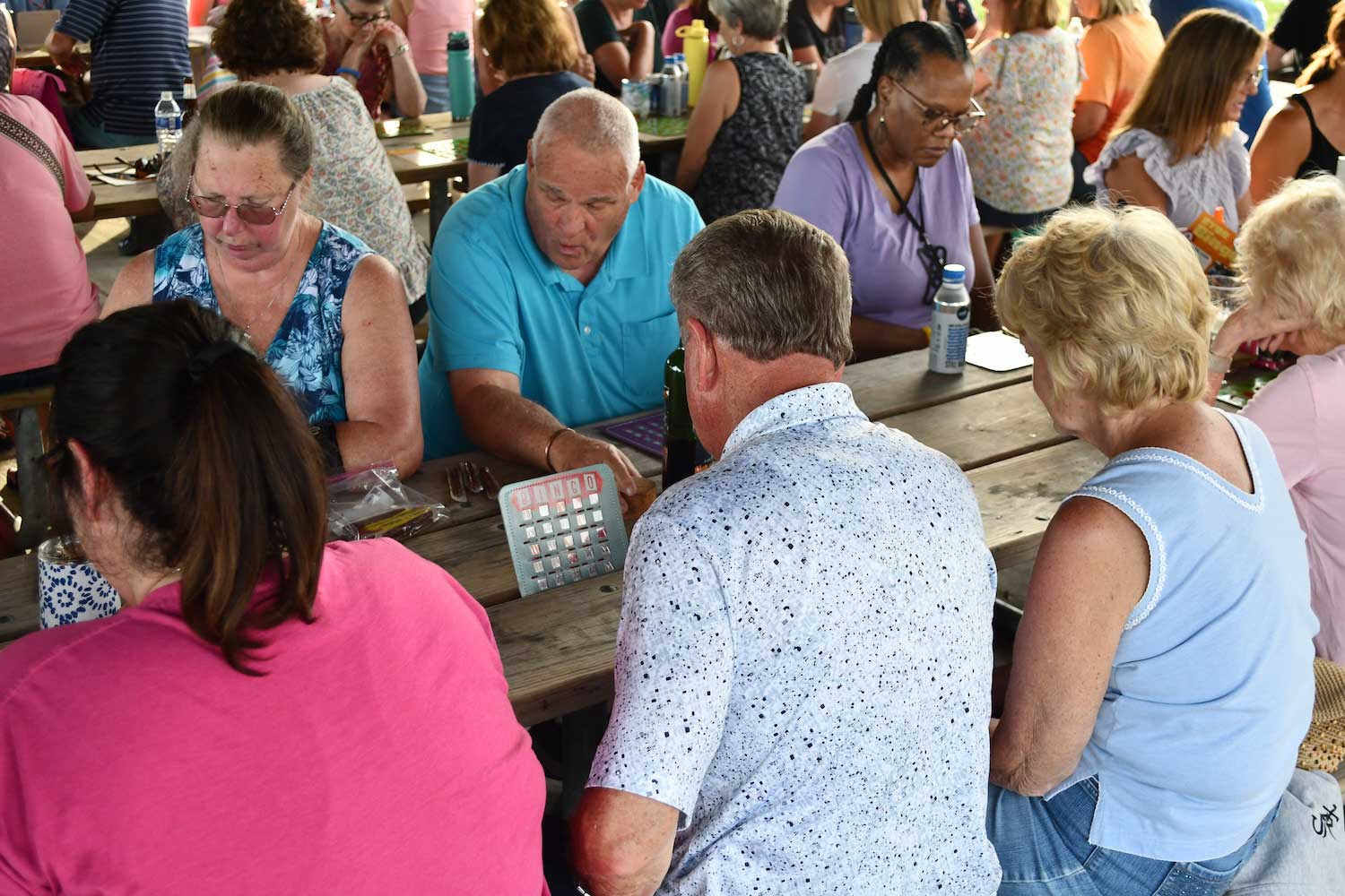 People sitting at wooden picnic tables playing bingo.