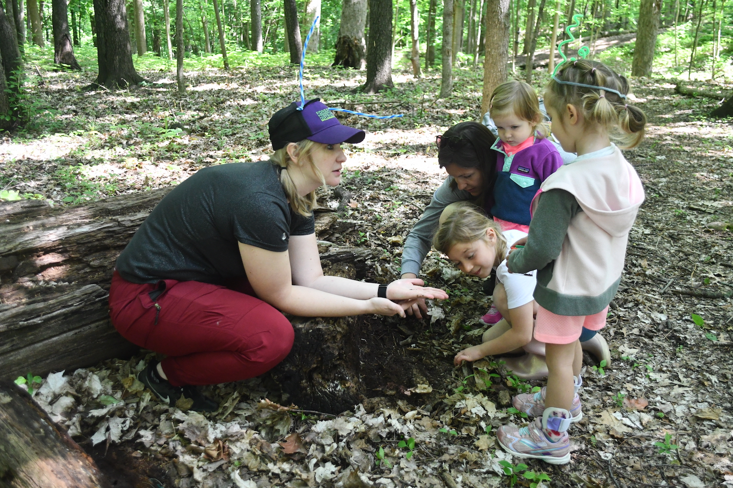 An adult crouched down on the ground showing a group of three kids and one adult something in their hands.