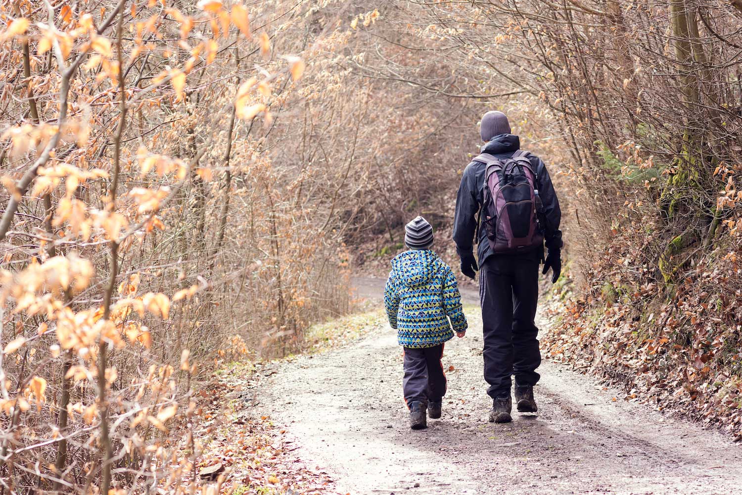 An adult and child walking along a snowy trail.