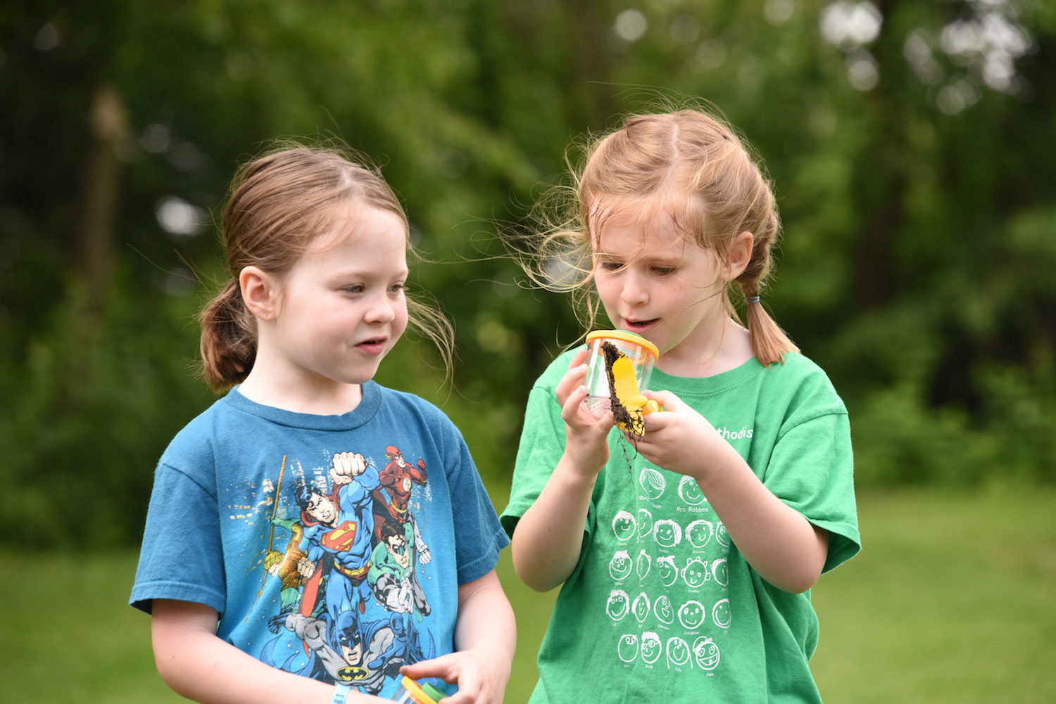 Two young girls looking with wonder and an insect in an insect jar.