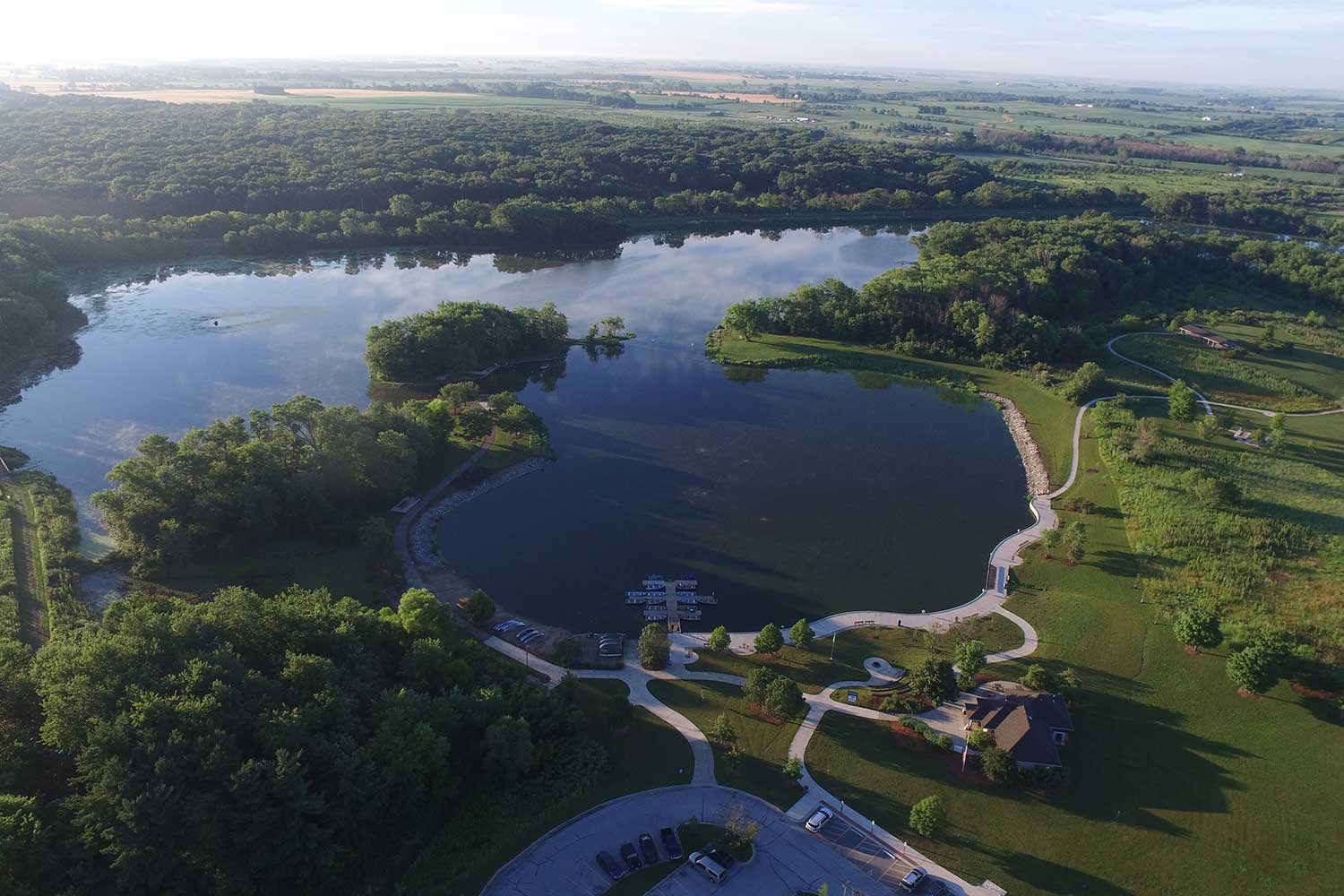 An aerial photo of a lake surrounded by green trees and grasses.