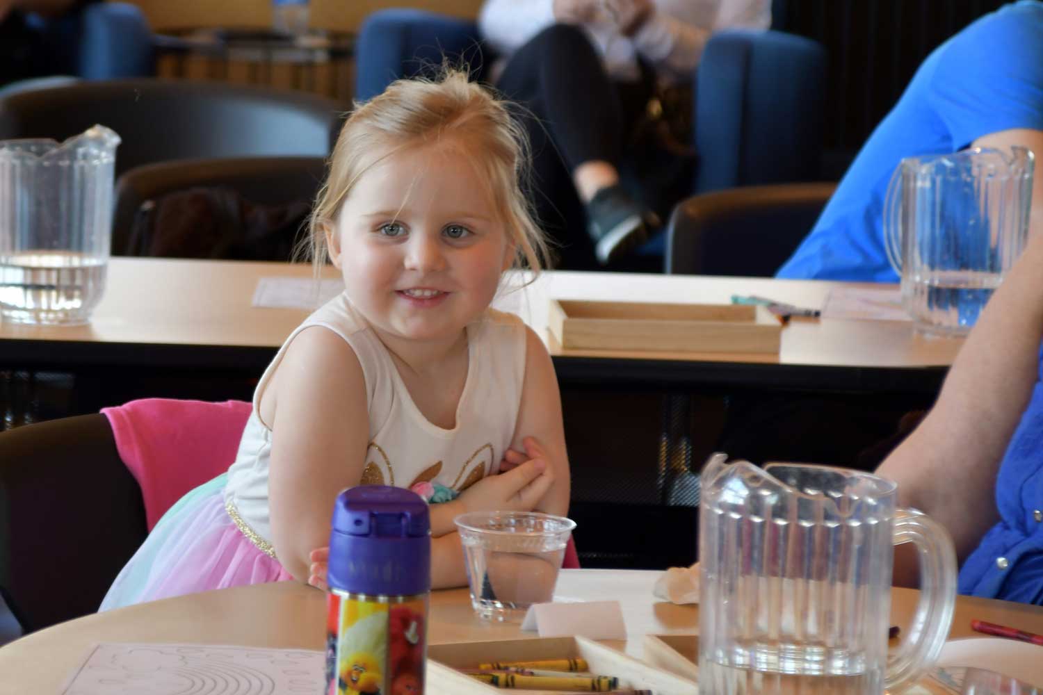 A young child smiling while leaning against a table.