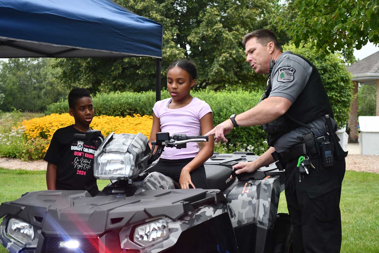 A police officer showing two kids a police all-terrain vehicle. One child is sitting on the ATV.