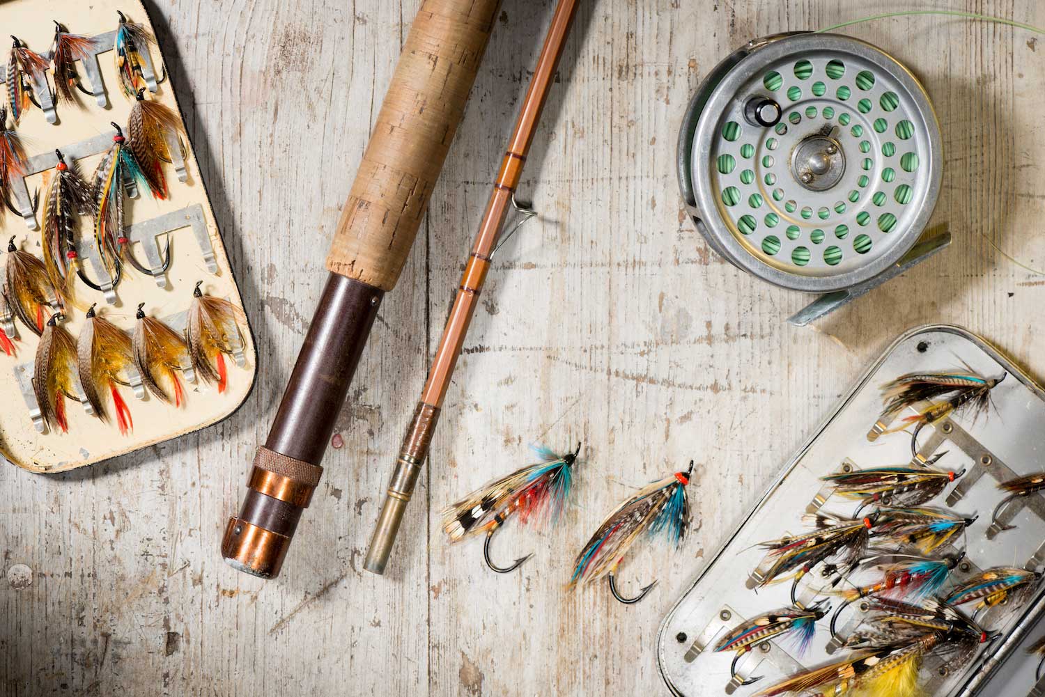 Fly-fishing lures and a fly-fishing rod on a wooden surface. 