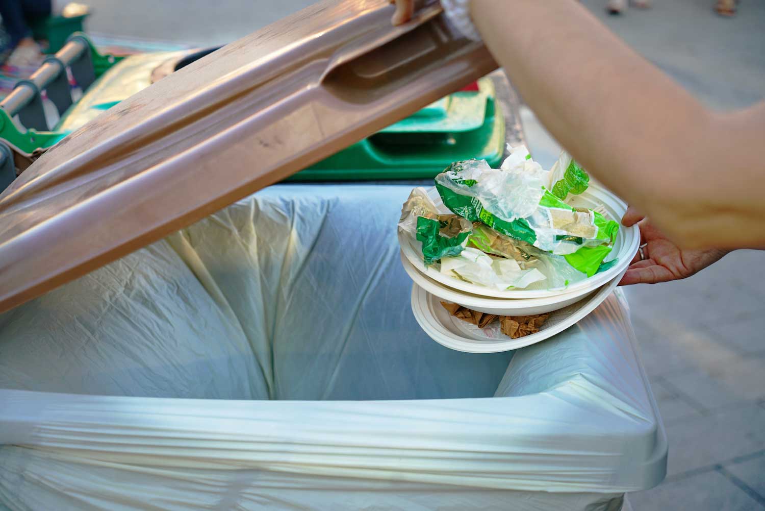 A hand throwing away trash in a garbage can.