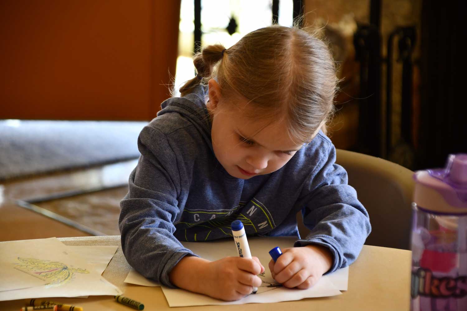 A young child sitting at a table while drawing with a marker.