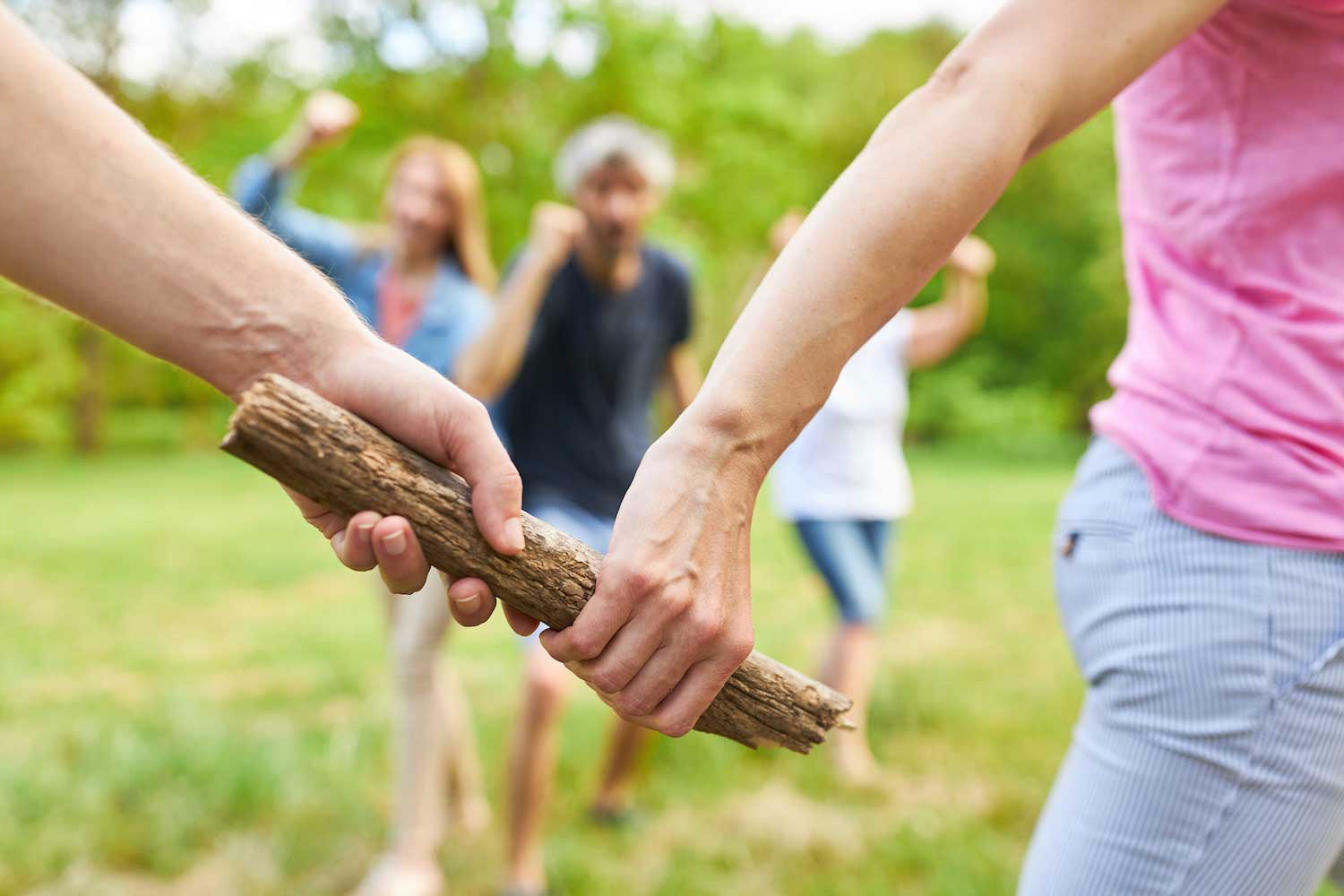 Two people exchanging a wooden stick as a baton while running the grass.