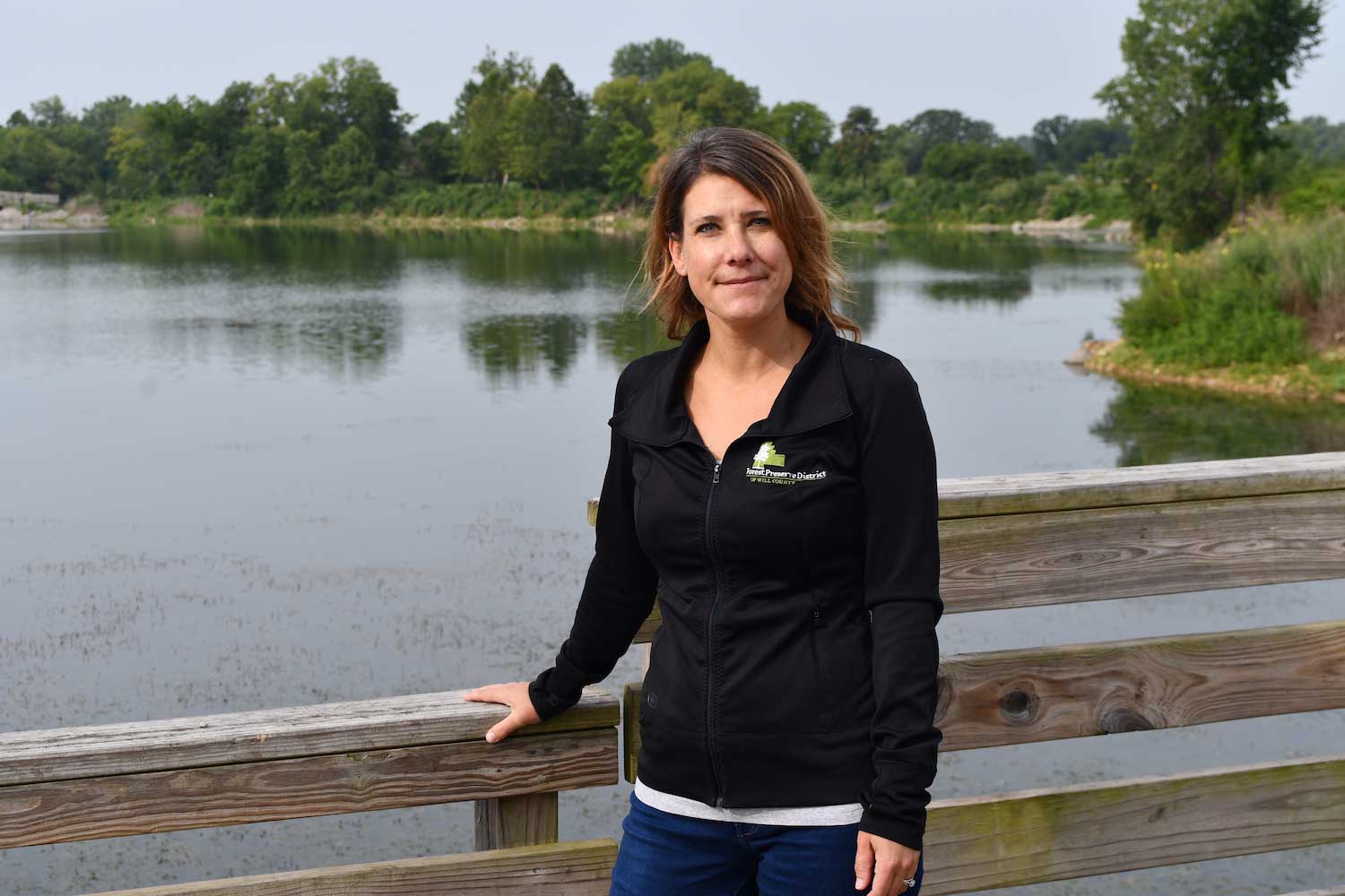 A person standing on a wooden bridge with a lake in the background.