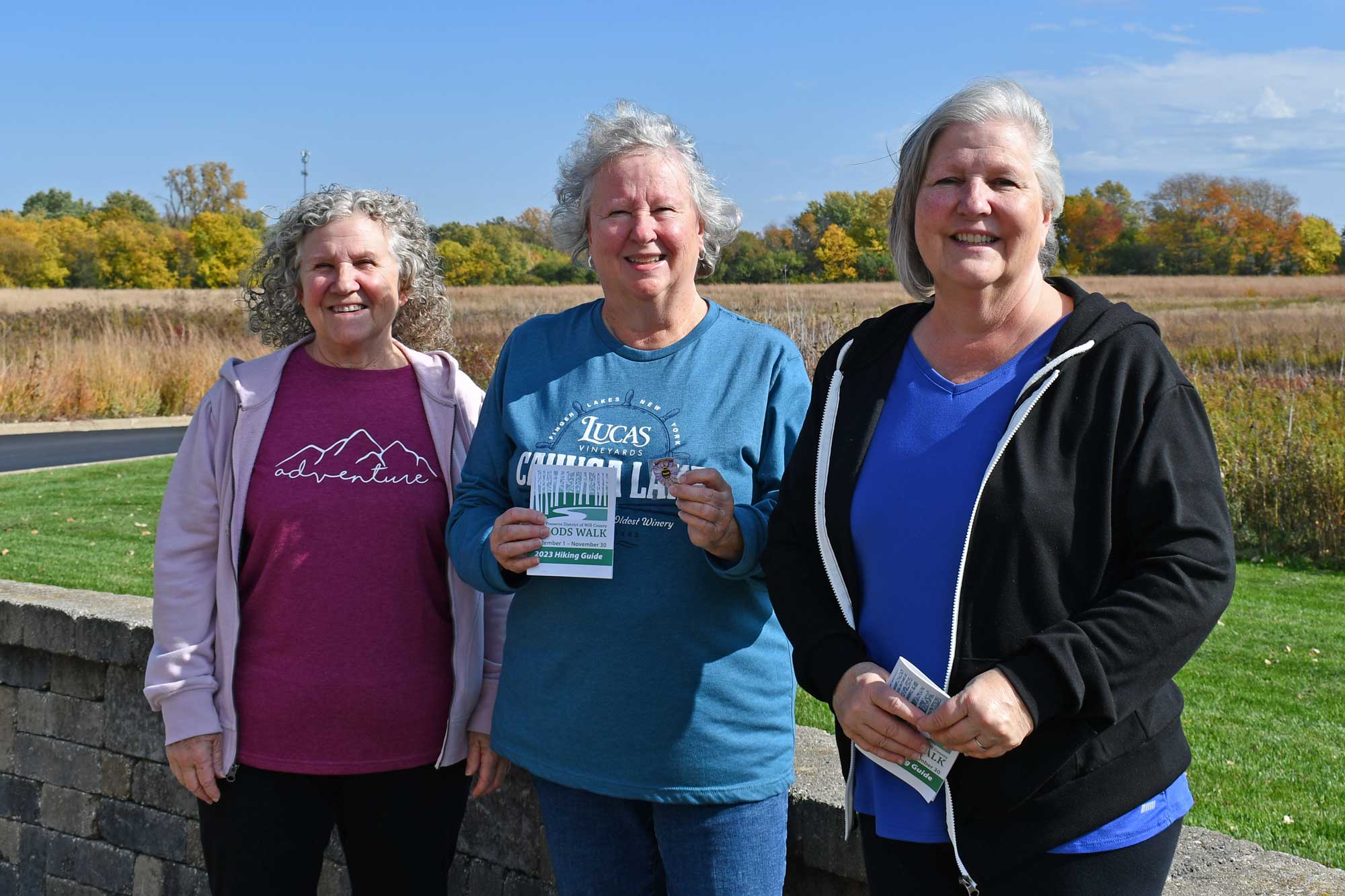 Three women pose outside near a trail.