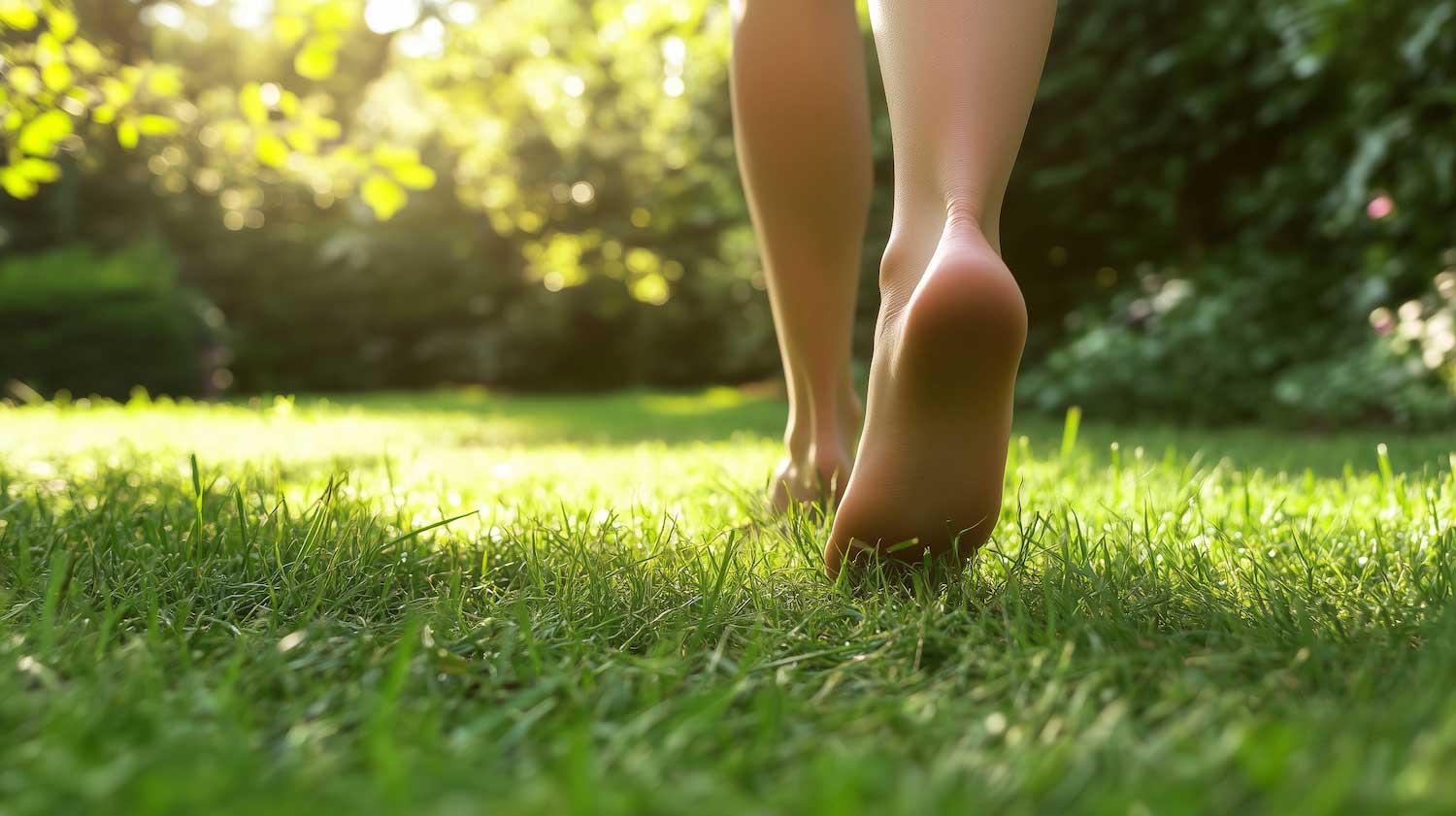 A person seen from the knee down walking through the grass with bare feet.