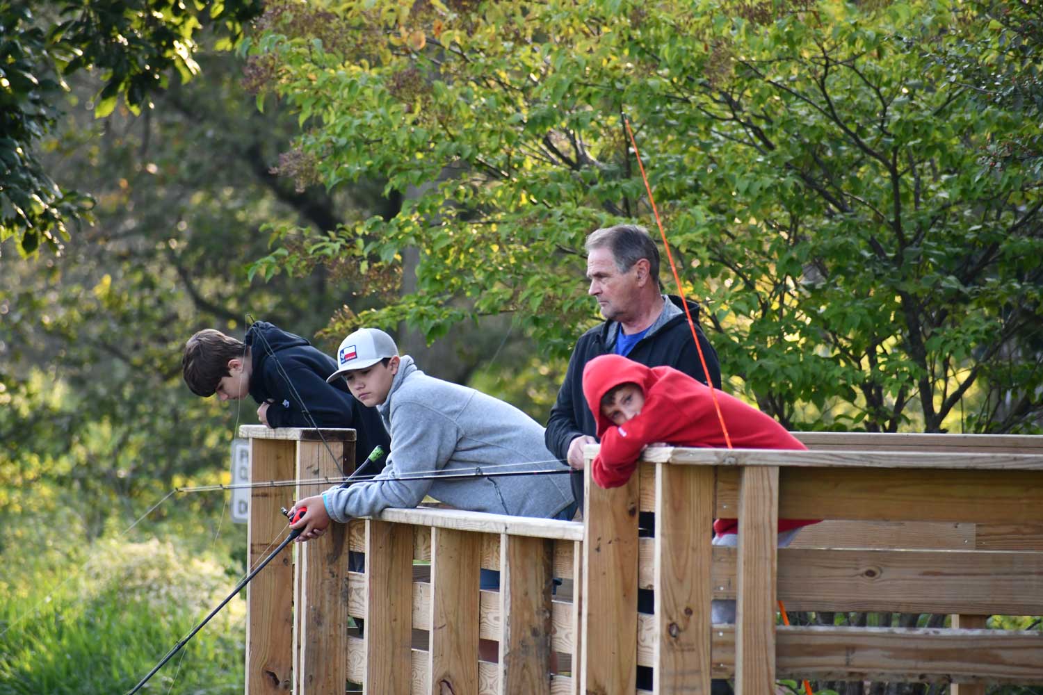 A group of four people standing on a wooden fishing dock with lines cast.