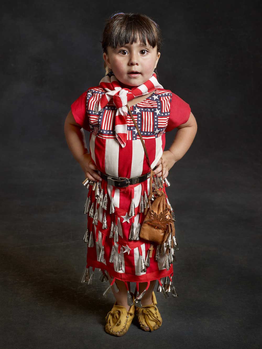 A child wearing traditional Potawatomi dress against a gray background.