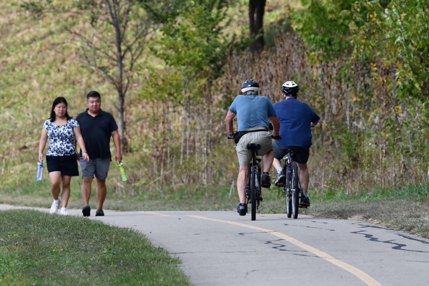 Two people walking and two people biking on a paved trail.