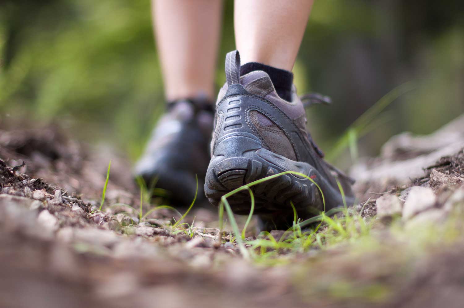 Feet in hiking boot walking along a natural surface trail.