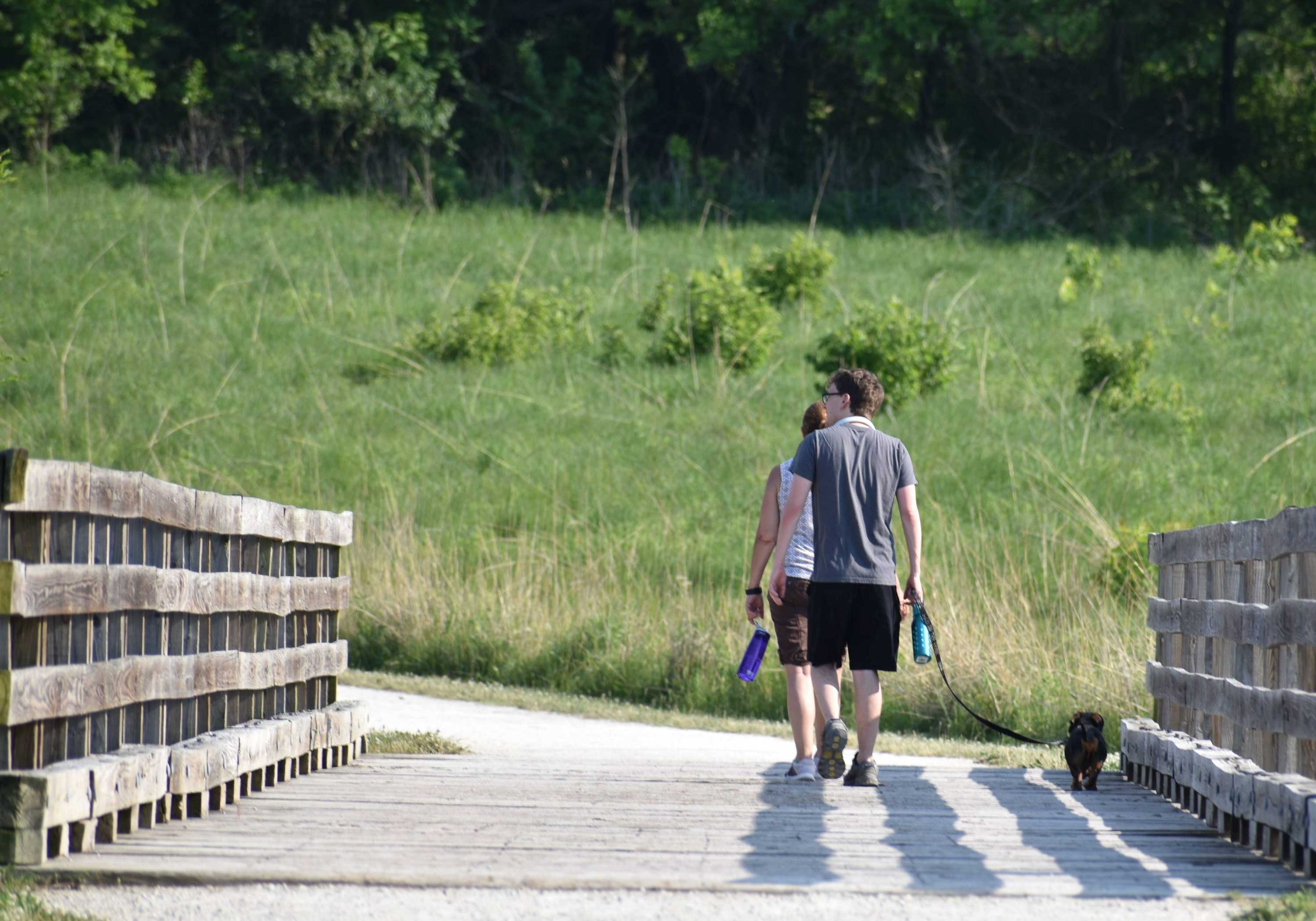 Couple walking their dog on a wooden bridge along a scenic nature trail.
