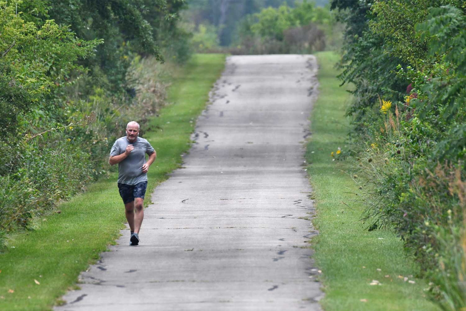 Person running on a paved trail lines with grasses and trees.