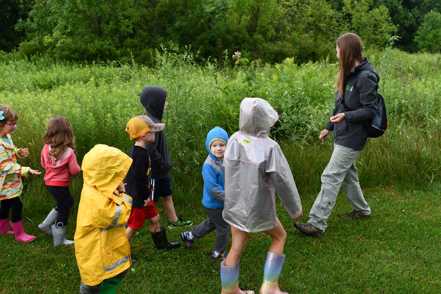An adult leading a group of kids on a walk along a prairie.