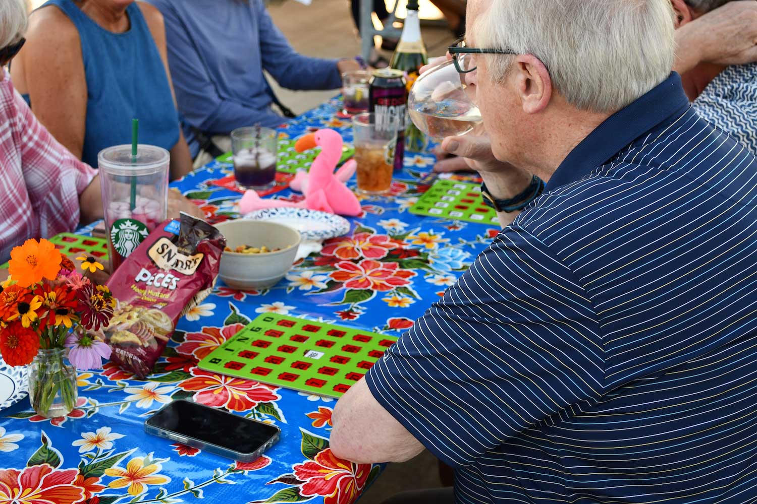 A group sitting around a picnic table enjoying drinks and food while playing bingo.