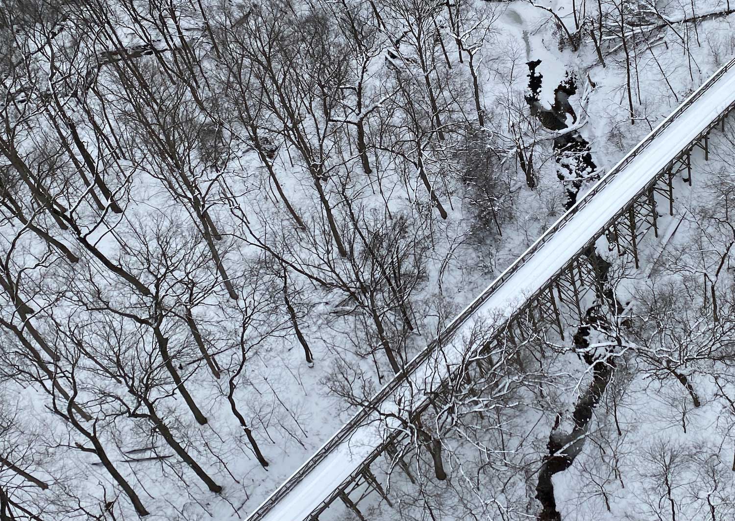 An aerial view of a snow-covered bridge in a forest.