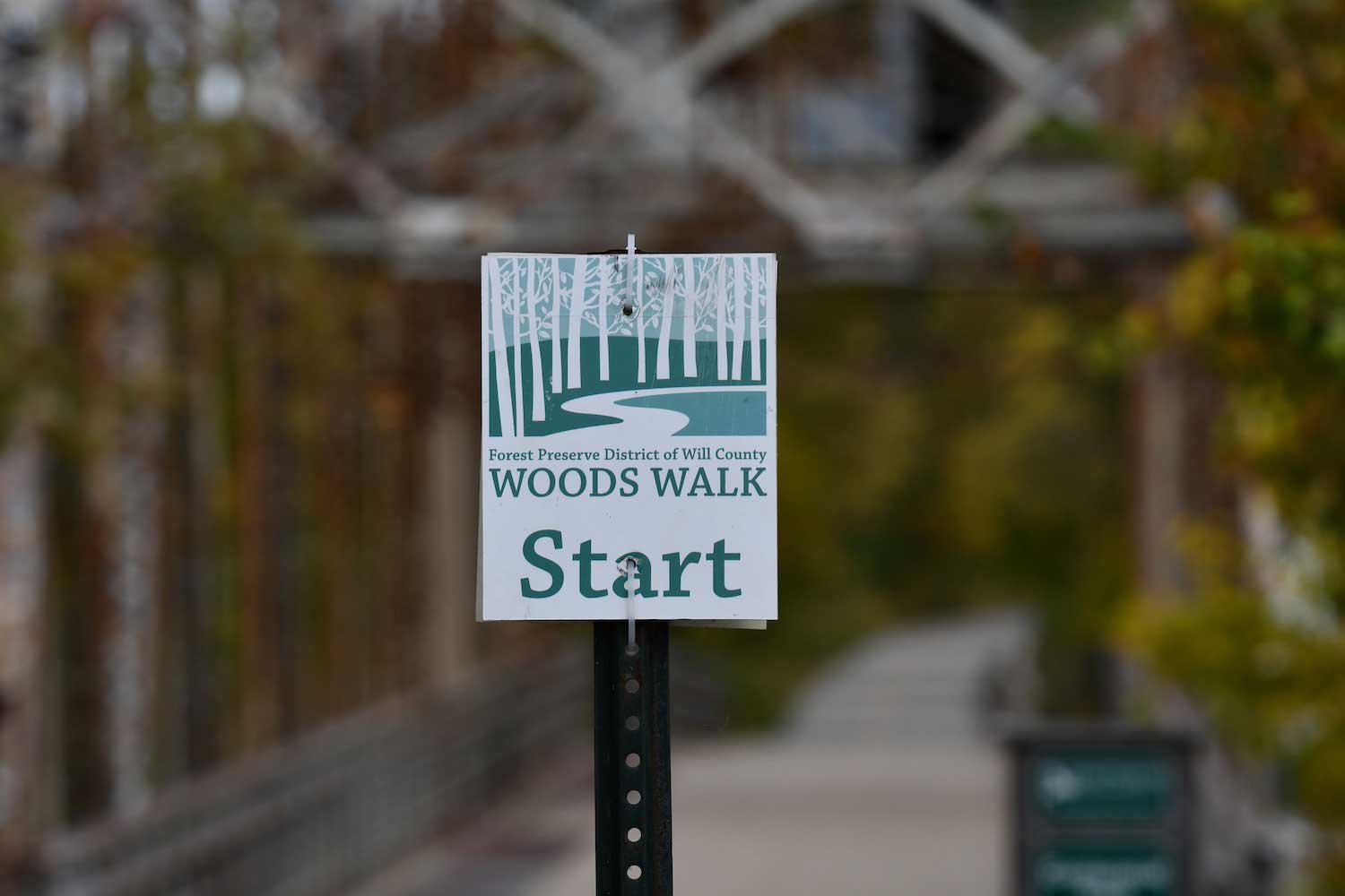 A Woods Walk sign along a trail in front of a bridge.