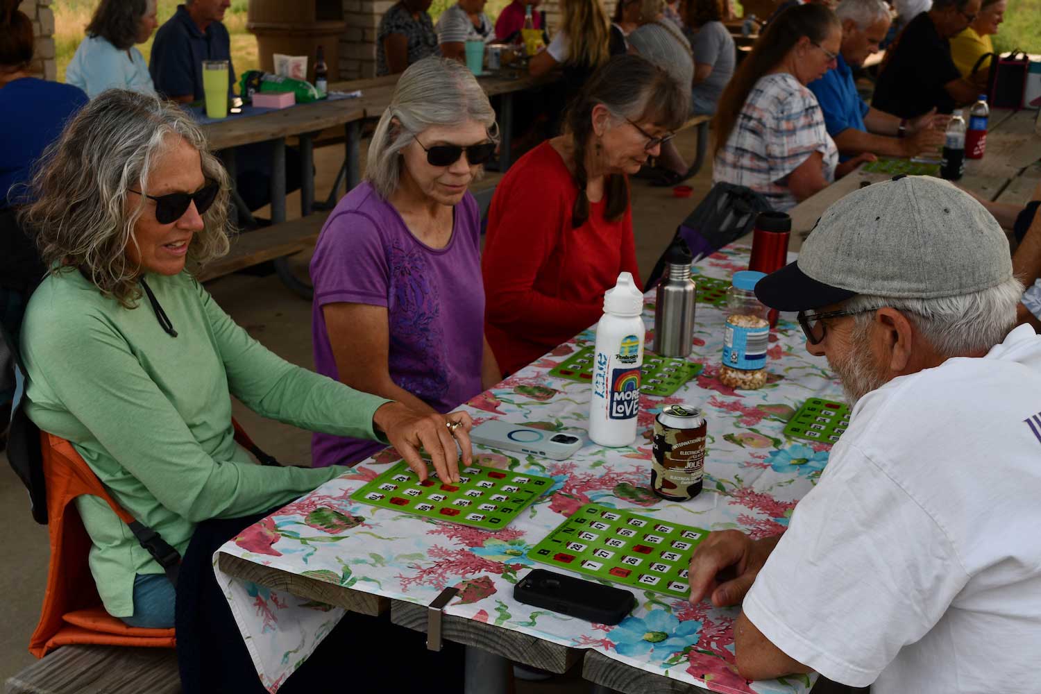 People sitting outdoors at picnic tables playing bingo.