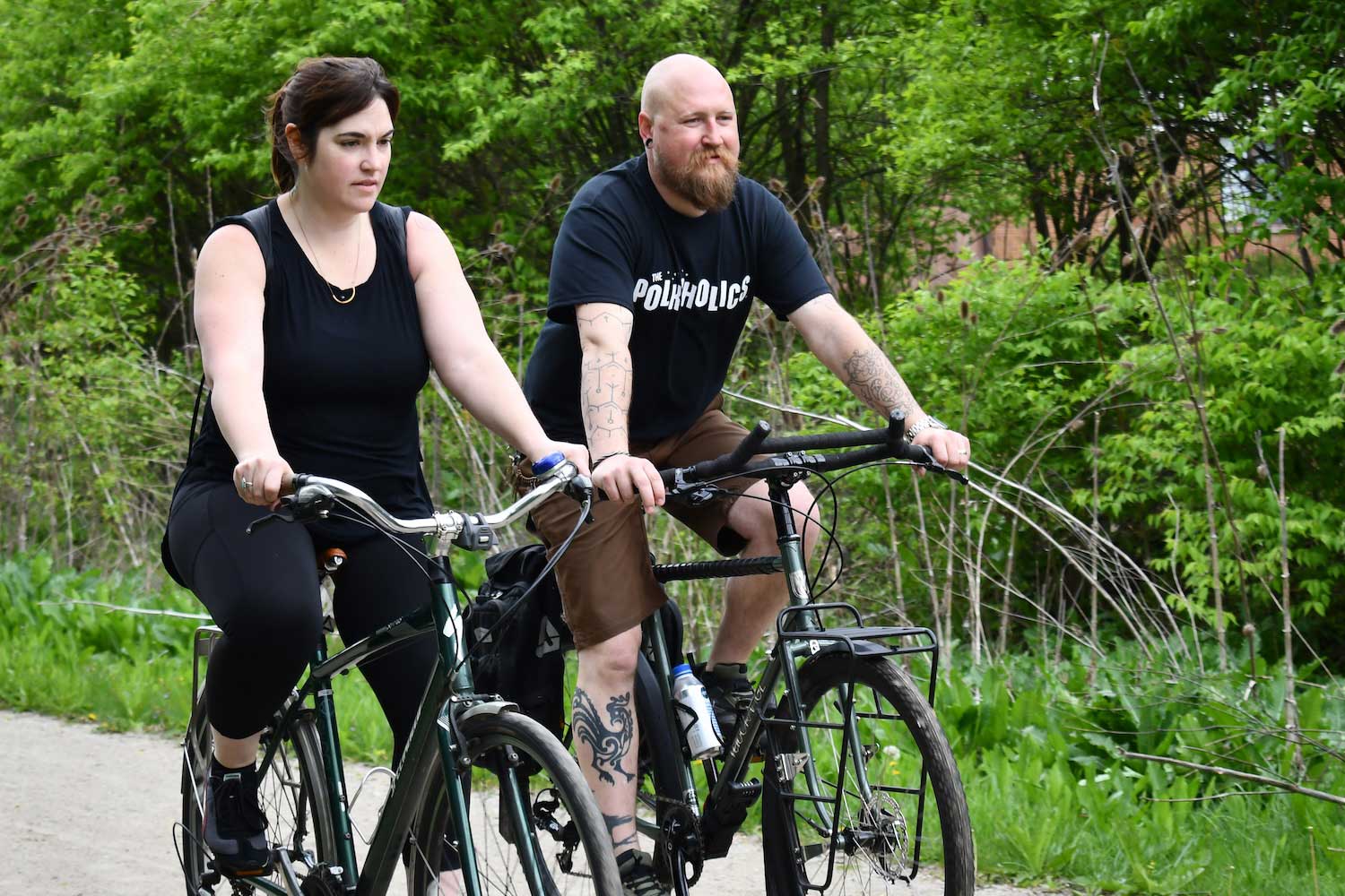 Two people biking side by side on a trail with trees in the background.