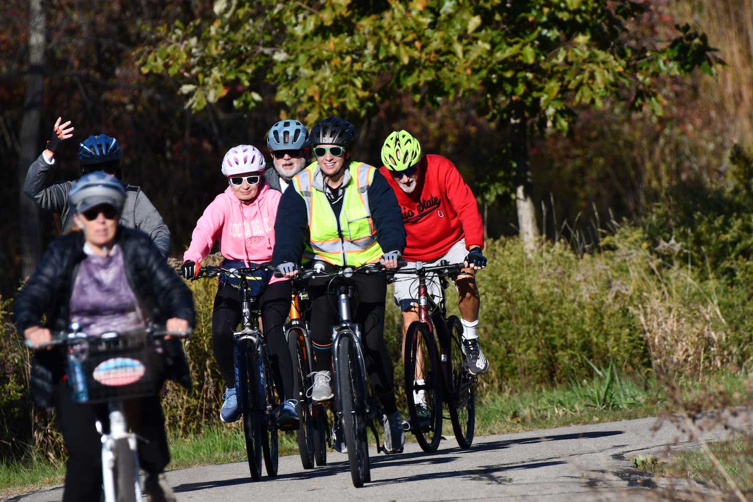 A group of six people wearing bike helmets riding bikes along a paved trail. 
