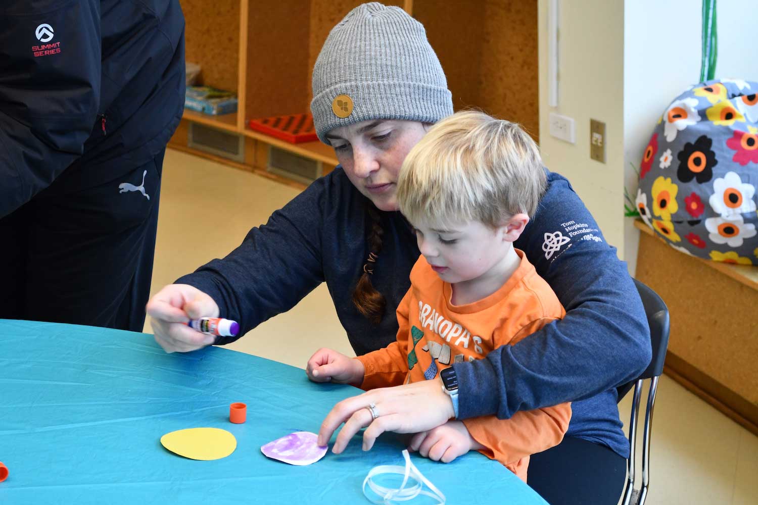 An adult helping a child with a craft project while sitting at a table.