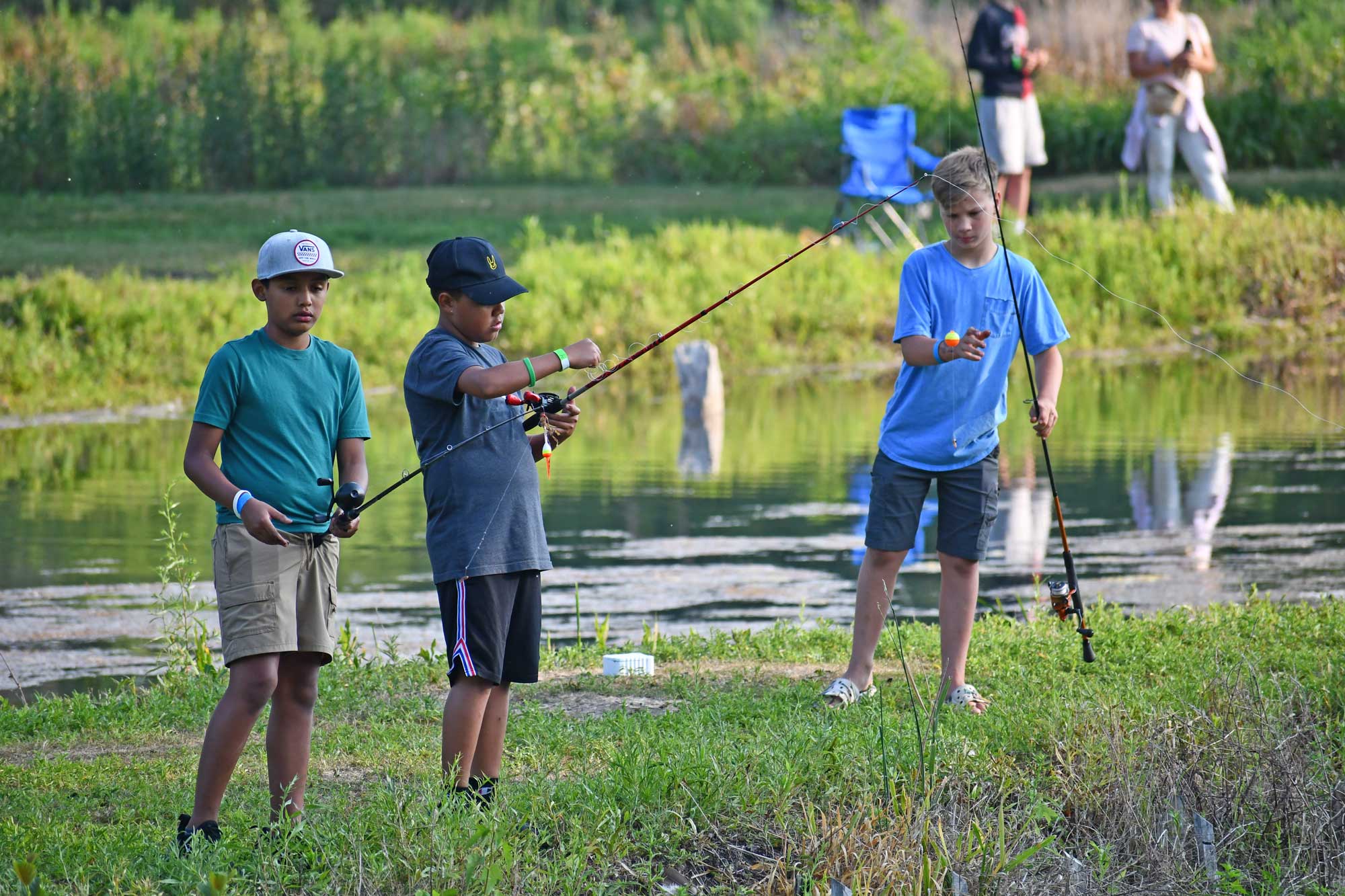 Three boys cast a line while fishing in a pond.