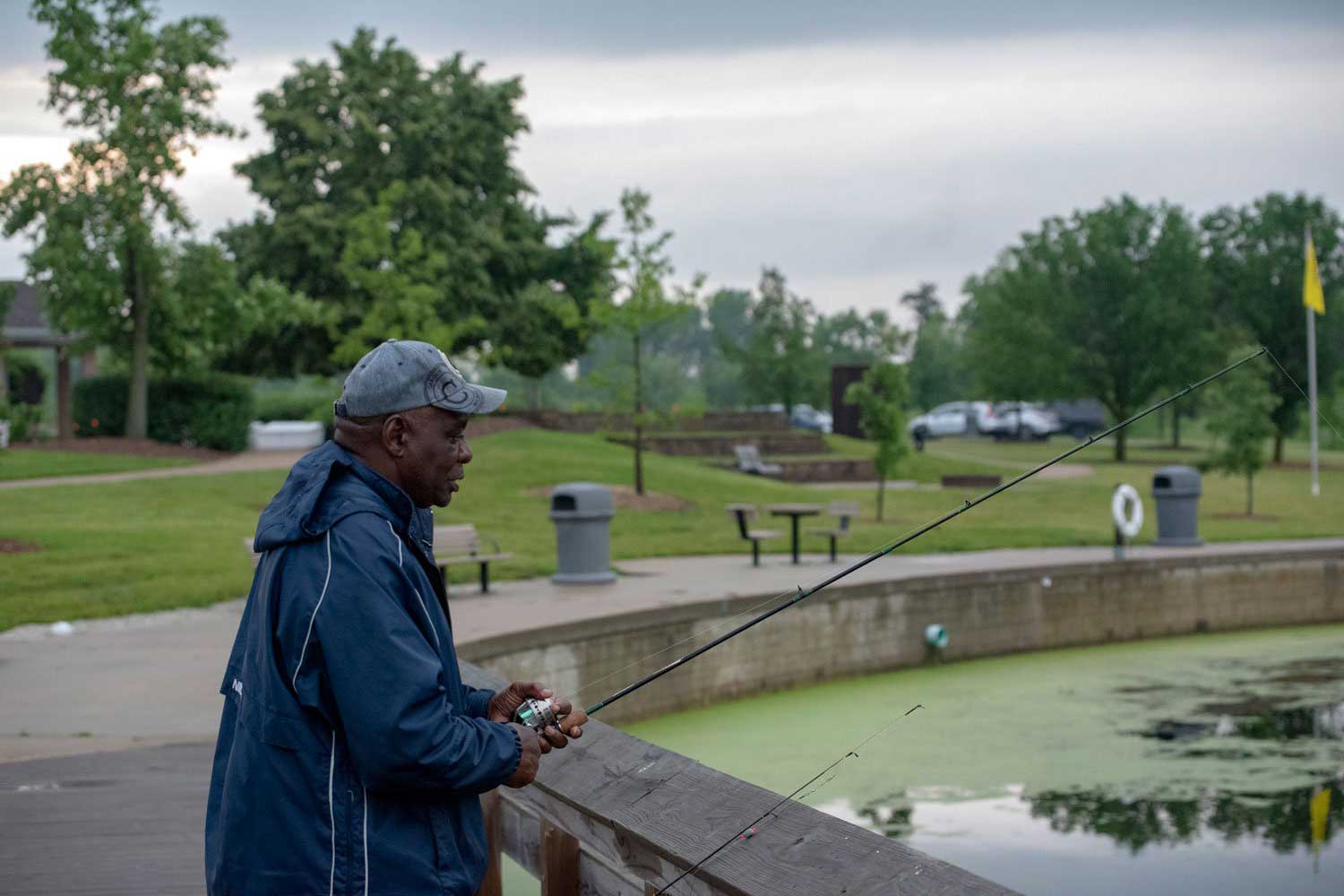 A person fishing along a wooden fence along the shoreline of a lake.