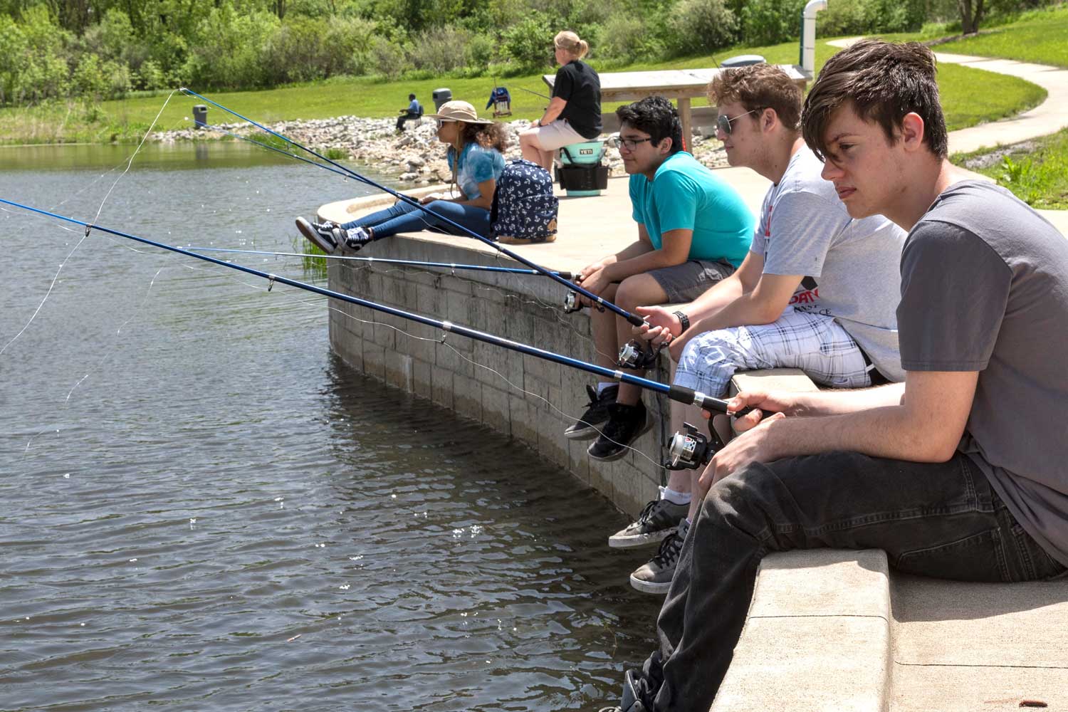 Group of people sitting on the edge of sidewalk while fishing.