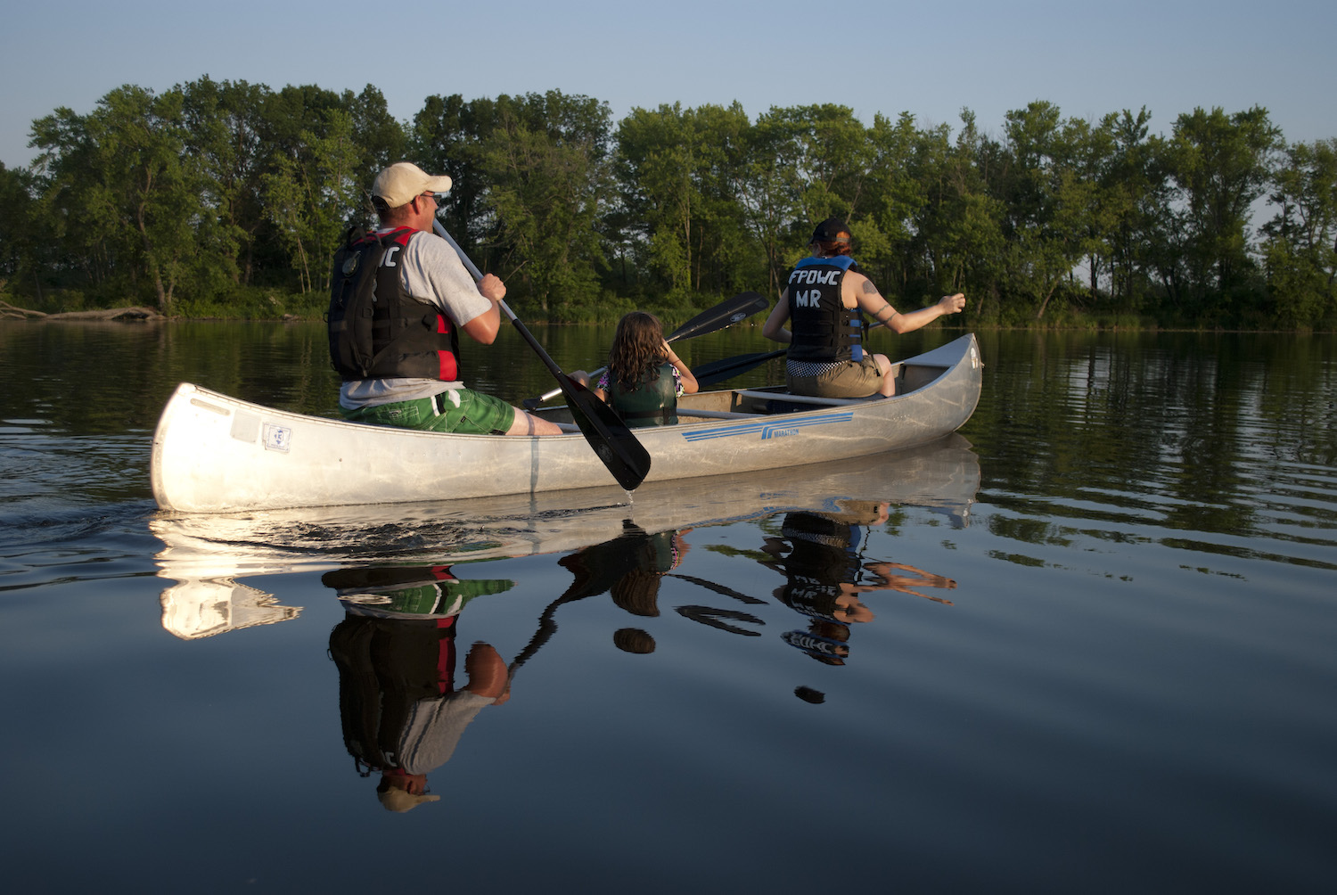 Two adults and a child paddling a canoe across a lake,