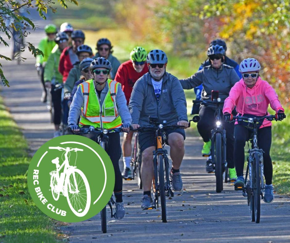 A group of about a dozen people in bike helmets riding bikes down a paved trail.