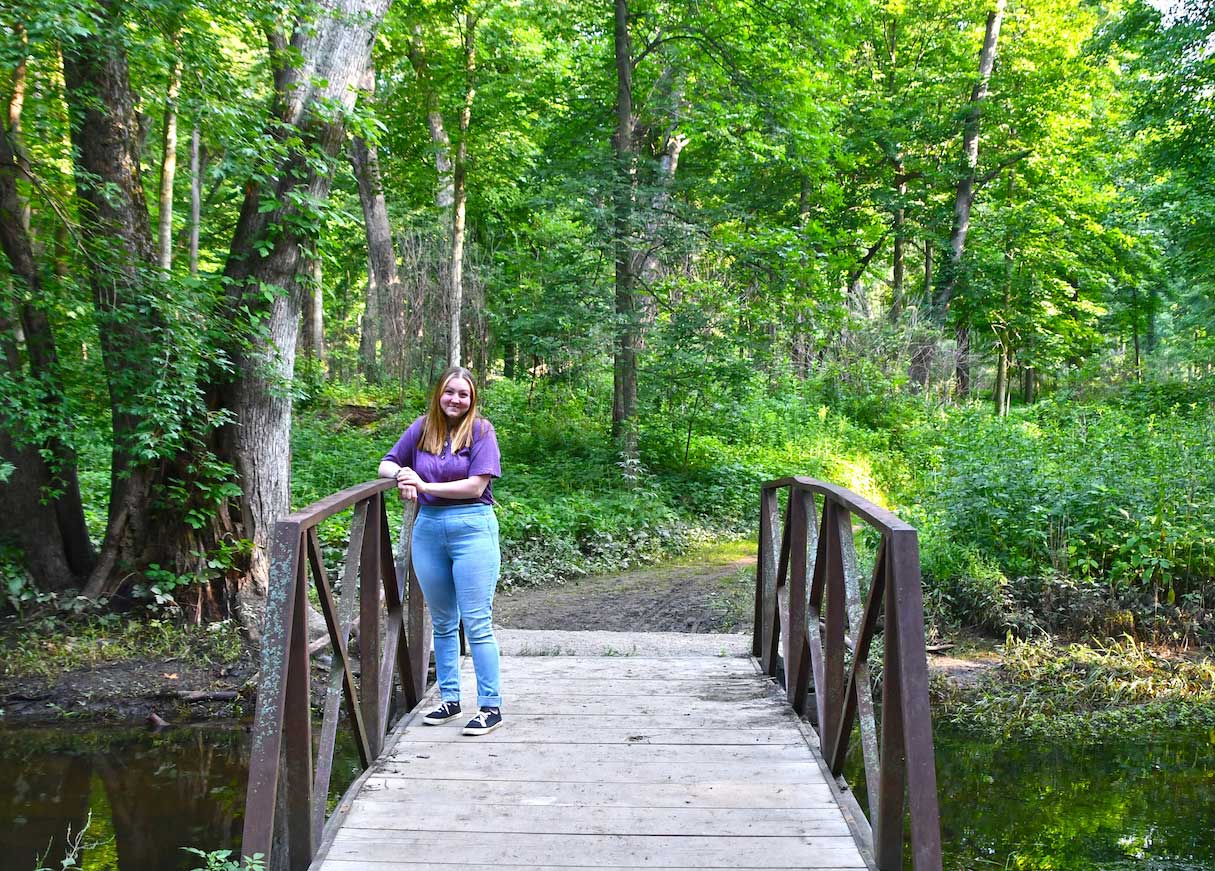 A person standing on a bridge over a creek in the woods.