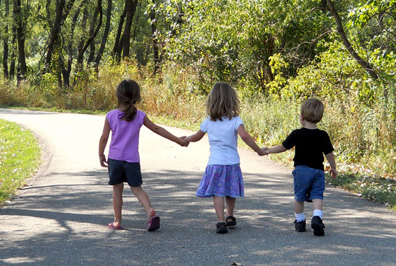 Two girls and a boy holding hands while walking in a trail.