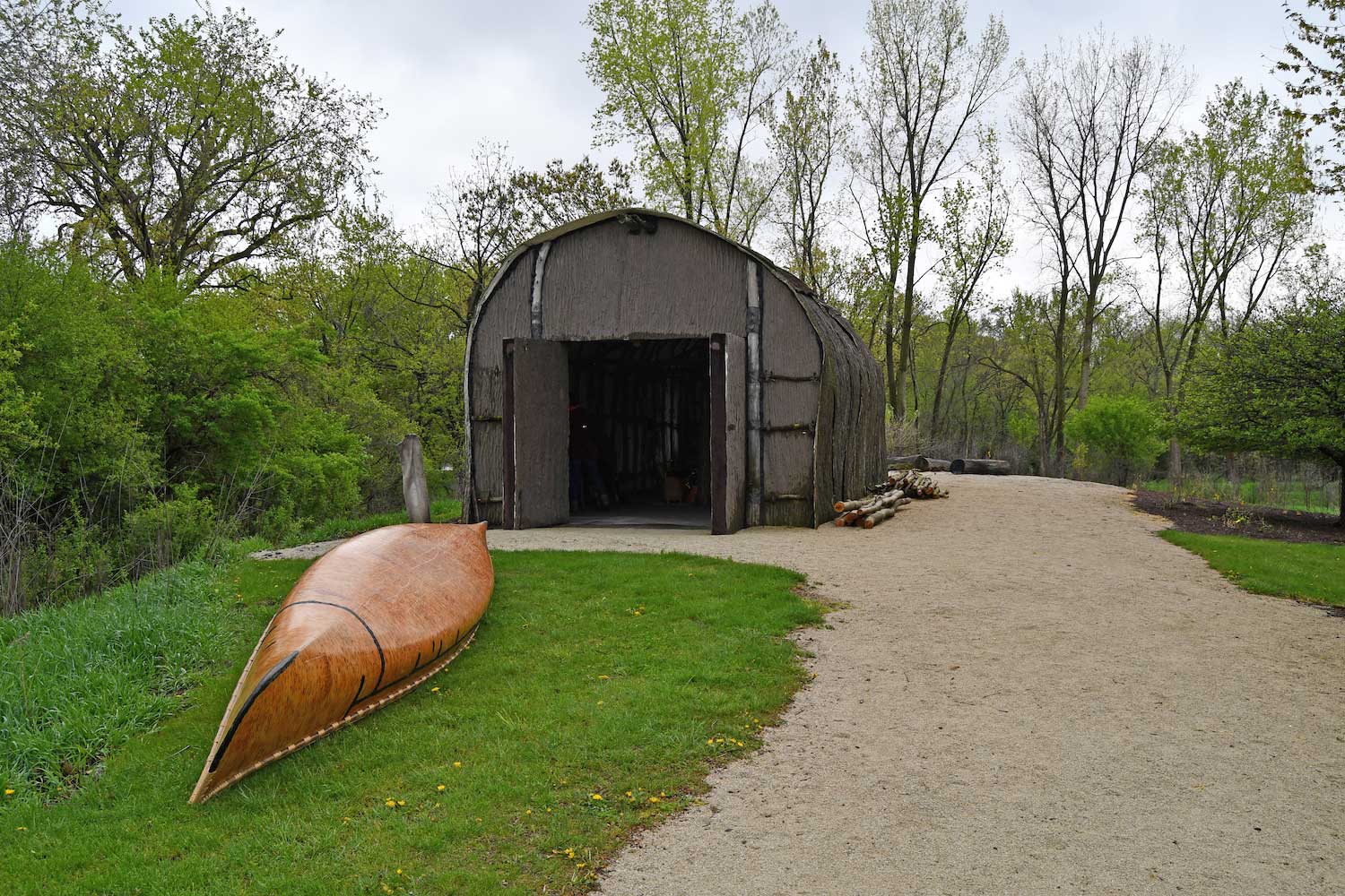 A Native American longhouse with a canoe sitting outside.