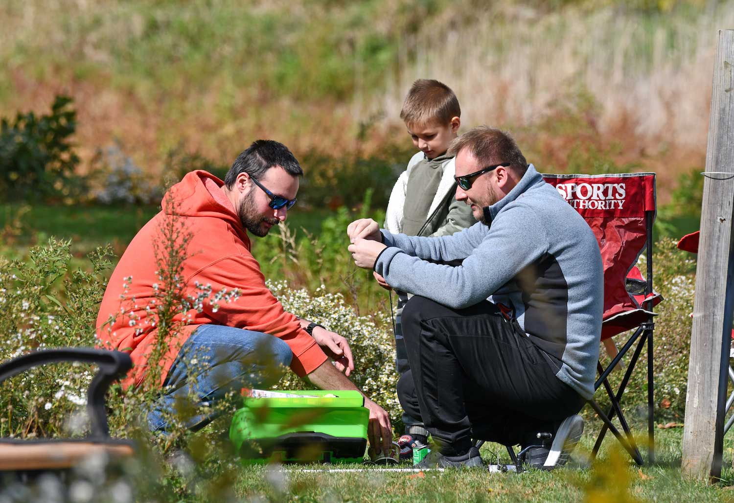 Two men and a boy crouched around a tackle box while prepping fishing poles.